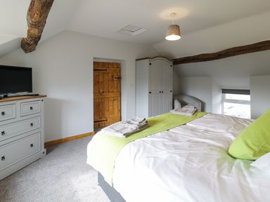 A bedroom with a bed green runner and pillows a white wardrobe a gray chest of drawers a wooden door and exposed wooden beams at Bryndan in Machynlleth