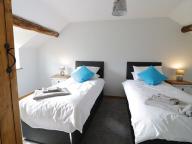 A bedroom with two single beds each with a blue pillow bedside tables with lamps and folded towels at Bryndan in Machynlleth