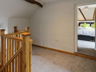 A hallway with wooden staircase railings and a bedroom with a bed and green pillows at Bryndan in Machynlleth