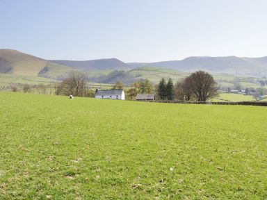 A green grassy field with a white house and trees with hills in the background at Bryndan in Machynlleth