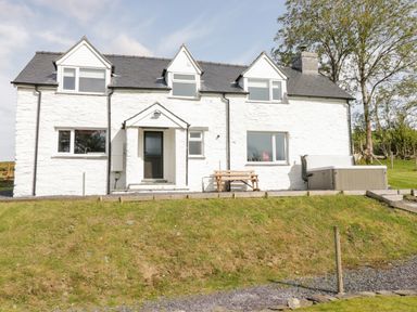 A white two-story house with a black door wooden bench and hot tub in a grassy yard at Bryndan in Machynlleth