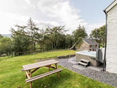A backyard with a wooden picnic table and a hot tub beside a white building at Bryndan in Machynlleth