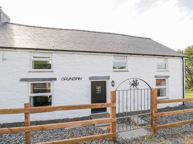 Exterior of a white stone house with black door and windows behind a wooden fence with metal gate at Bryndan in Machynlleth