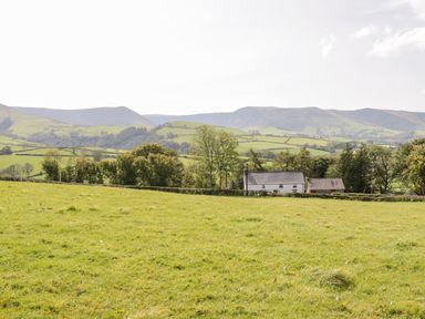 A landscape with green fields trees a white house and distant hills at Bryndan in Machynlleth