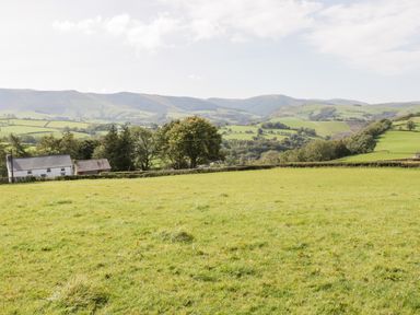 A green field with a white house and trees with hills in the background at Bryndan in Machynlleth