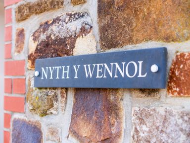 A nameplate reading NYTH Y WENNOL on a stone wall at Nyth Y Wennol in Abersoch
