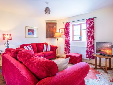 A living room with red sofas a wooden table with a television floral curtains and a window at Nyth Y Wennol in Abersoch