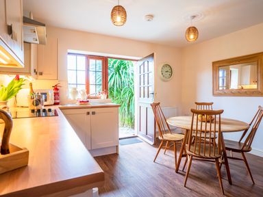 A kitchen with wooden table and chairs and an open door showing greenery outside at Nyth Y Wennol in Abersoch