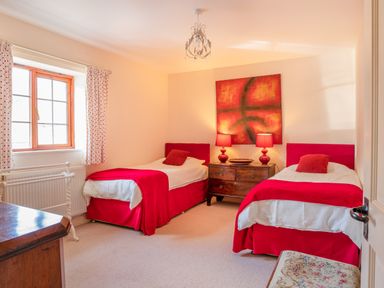 A bedroom with two single beds a wooden dresser and a window with curtains at Nyth Y Wennol in Abersoch