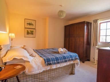 A bedroom with a bed covered with pillows and a blue blanket next to a wooden wardrobe and a window at Nyth Y Wennol in Abersoch