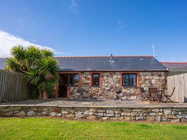 A stone exterior cottage with a slate roof a wooden fence and outdoor furniture in a garden at Nyth Y Wennol in Abersoch