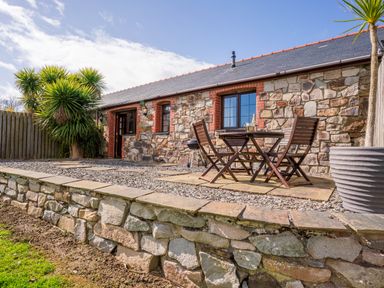A stone building with a slate roof and a patio area with wooden table and chairs and plants at Nyth Y Wennol in Abersoch