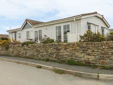 A single-story white house with a stone wall and plants along the sidewalk at 11 Pendarves in St Merryn near Padstow