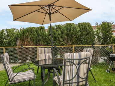 A garden with a round glass table and four striped cushioned chairs under a large umbrella at 11 Pendarves St Merryn near Padstow