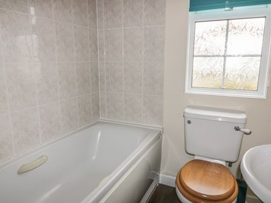 A bathroom with a bathtub, toilet with wooden seat, and a window with frosted glass at 11 Pendarves in St Merryn near Padstow
