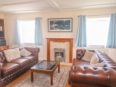 A living room with two brown leather sofas a glass coffee table a fireplace and two windows with blue curtains at 11 Pendarves St Merryn near Padstow