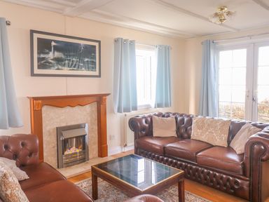A living room with brown leather sofas a fireplace a coffee table and light blue curtains at 11 Pendarves in St Merryn near Padstow