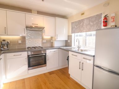 A kitchen with white cabinets a gas stove an oven a sink a coffee machine and a refrigerator at 11 Pendarves St Merryn near Padstow