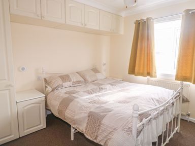 A bedroom with a double bed covered in patchwork bedding a window with curtains and built in overhead cupboards at 11 Pendarves St Merryn near Padstow