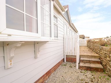 An exterior side pathway with gravel and steps next to a white house and stone wall at 11 Pendarves St Merryn near Padstow