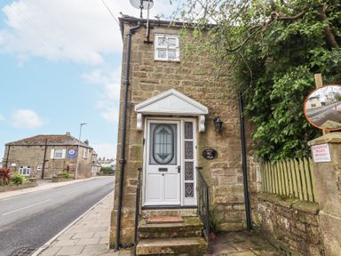 Stone house with white door and steps on a street next to a green fence with a no parking sign at Edendale in Longframlington near Alnwick