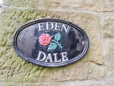 A stone wall with an oval black sign displaying a red rose and the words Eden Dale