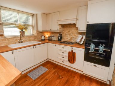 A kitchen with white cabinets wooden countertops a sink a window with blinds a black oven and stove and various kitchen utensils at Edendale Longframlington near Alnwick