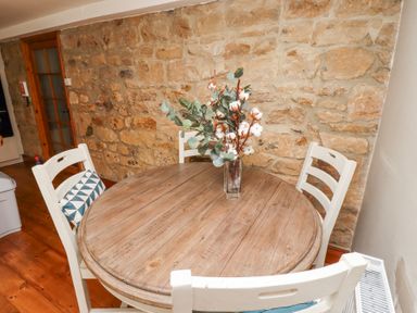 A round wooden table with a vase of flowers and four white chairs against a stone wall at Edendale in Longframlington near Alnwick