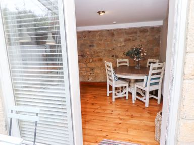 A dining area with a round wooden table and four white chairs with cushions against a stone wall at Edendale Longframlington near Alnwick