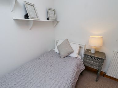 A small bedroom with a single bed grey blanket and pillows a bedside table with a lamp and a white wall shelf with two picture frames at Edendale in Longframlington near Alnwick