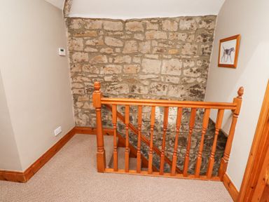 A stairway with a wooden banister stone wall and framed dog picture at Edendale in Longframlington near Alnwick