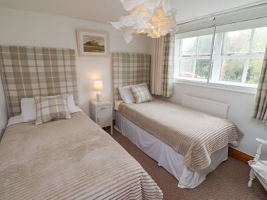 A bedroom with two single beds a bedside table with a lamp and a window with curtains at Edendale Longframlington near Alnwick