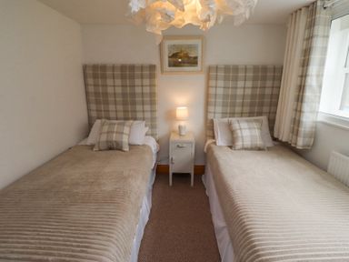 A bedroom with two single beds with plaid headboards and matching cushions a nightstand and lamp between the beds and a window with plaid curtains at Edendale in Longframlington near Alnwick