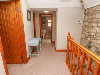 A carpeted hallway with wooden doors a small blue table a stone wall and a bathroom visible at Edendale in Longframlington near Alnwick