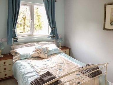 A bedroom with a double bed blue curtains and bedside tables with lamps at Park Brook Retreat in Scorton