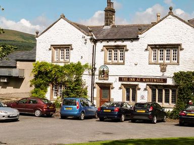 White building with multiple windows and cars parked in front at The Inn at Whitewell in Scorton