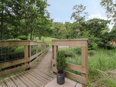 A wooden footbridge with railings over grassy land and trees at Park Brook Retreat in Scorton