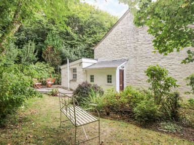 A garden with a metal bench and wooden chairs near a white stone building at Tinners Cottage in Liskeard