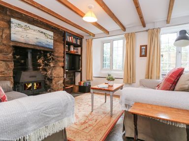 A living room with a stone fireplace two sofas a wooden coffee table bookshelf and windows at Tinners Cottage in Liskeard