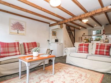 A living room with two sofas red plaid cushions a wooden coffee table and kitchen in the background at Tinners Cottage in Liskeard