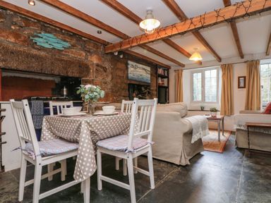 A dining area with a table and four chairs next to a living room with two sofas and a coffee table at Tinners Cottage in Liskeard