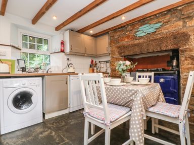 A kitchen with a dining table set for four and a blue stove in a stone fireplace at Tinners Cottage in Liskeard