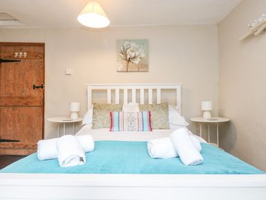 A bedroom with a white bed frame blue blanket rolled white towels and wooden door at Tinners Cottage in Liskeard