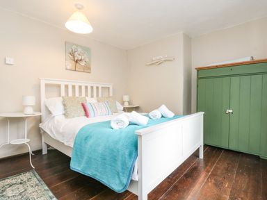 A bedroom with a white bed and green wardrobe with blue blanket and rolled towels at Tinners Cottage in Liskeard