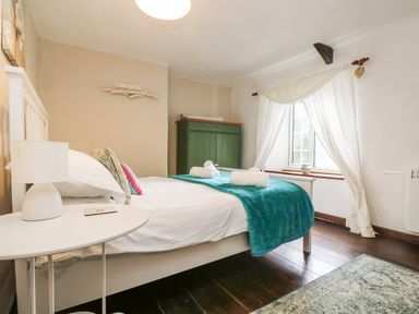 A bedroom with a white bed blue blanket white bedside table and green cabinet at Tinners Cottage in Liskeard