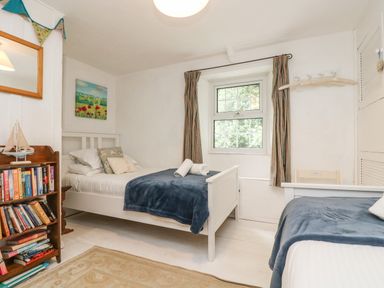 A bedroom with two single beds a bookshelf a window and a wall mirror at Tinners Cottage in Liskeard