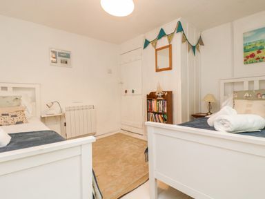 A bedroom with two white beds a rug and a bookshelf at Tinners Cottage in Liskeard