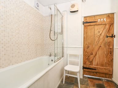A bathroom with a bathtub shower combination a white chair and a wooden door at Tinners Cottage in Liskeard