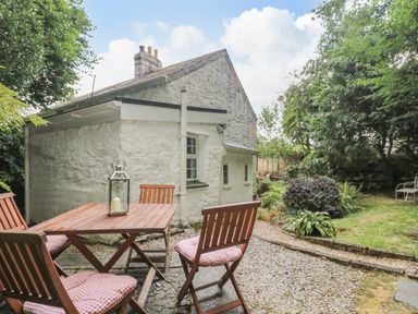 An outdoor patio with wooden chairs and table beside a white stone cottage in a garden at Tinners Cottage in Liskeard
