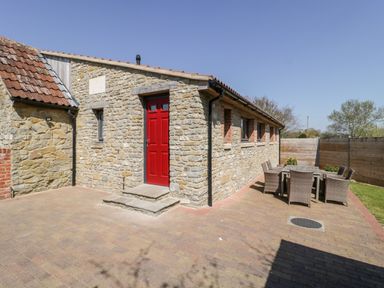 An outdoor patio area with a stone building featuring a red door and a table with chairs at The Stone Barn in Evercreech near Shepton Mallet